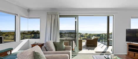A spacious living area with a balcony, large windows, and a flat-screen TV.