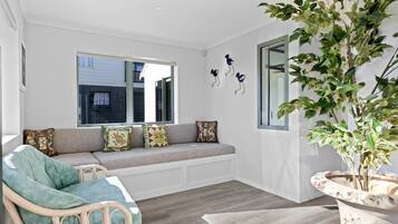 A room with a built-in bench, a wicker chair, a potted plant, and a window with a view.