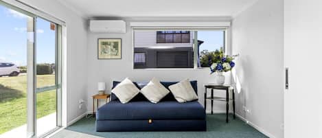 A room with a blue sofa, a small table with a vase, and a window with blinds.