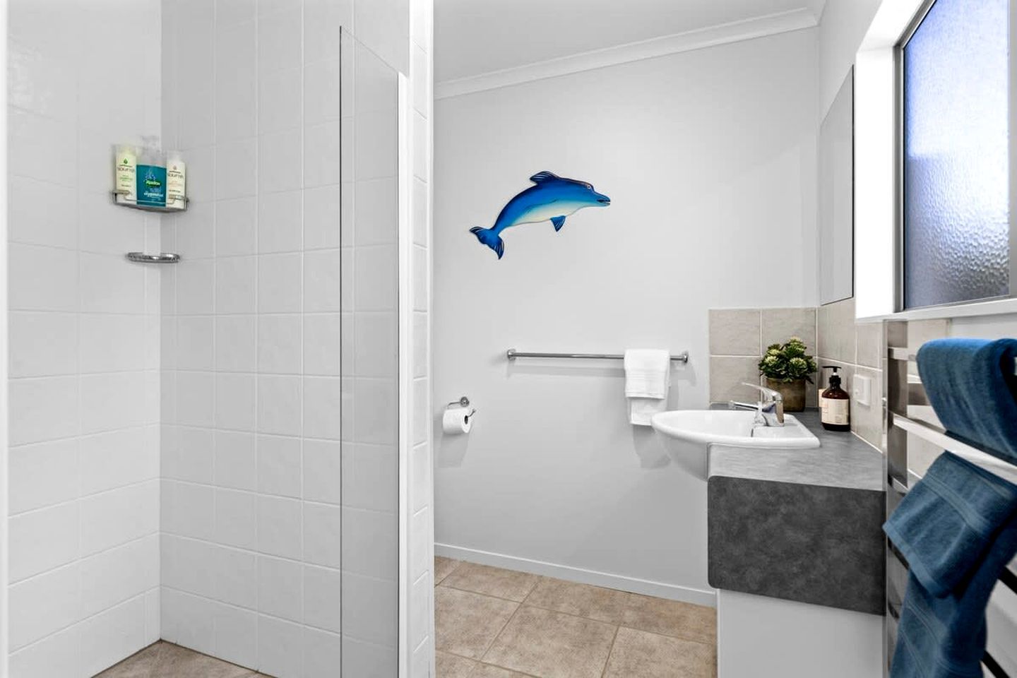 Une salle de bain avec une douche, des toilettes, un lavabo et une fresque représentant un dauphin sur le mur.