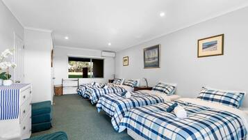A hotel room with four beds, a desk, a chair, a dresser, and a window with a view of greenery.