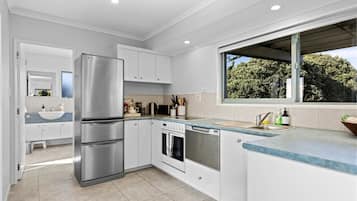 A modern kitchen with stainless steel appliances, white cabinetry, and a large window offering a view of greenery.