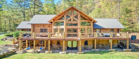 A log cabin with a deck, multiple windows, and a stone foundation.