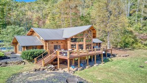 A log cabin with a deck, a staircase, and a view of the surrounding forest.