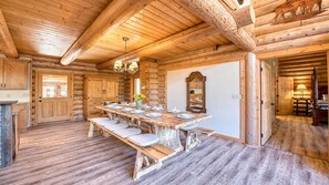 A log cabin interior with a large dining table, wooden walls, and a chandelier.