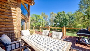 Una terraza de madera con una mesa, sillas, una parrilla y vistas a los árboles.