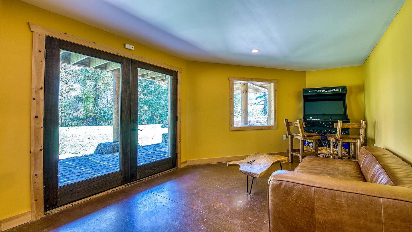 A room with a sliding glass door leading to an outdoor area, a wooden bench, a sofa, and a television.
