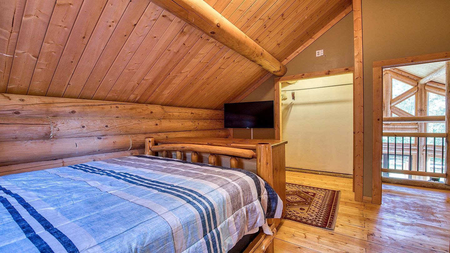 Ein Schlafzimmer einer Holzhütte mit Bett, Fernseher und Blick ins Freie.