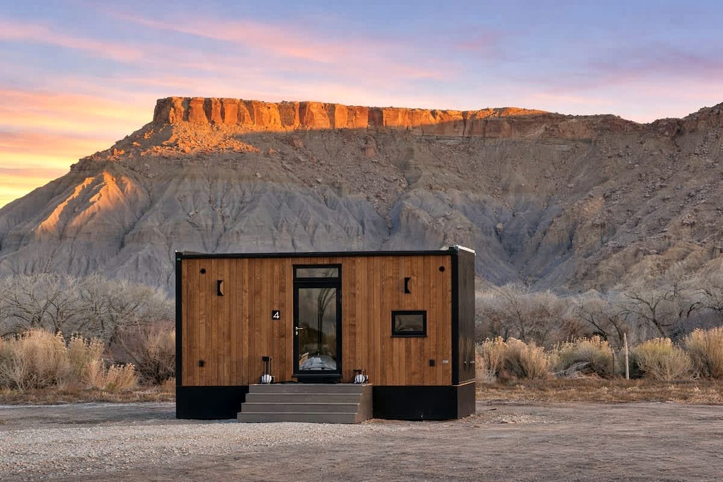 Une cabane en bois, dotée d’une porte et de fenêtres, se dressant sur fond de montagnes.