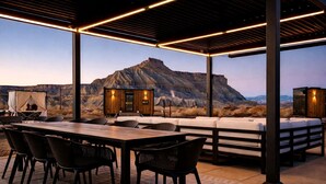 Eine Terrasse im Freien mit einem Holztisch und -stühlen, einer Sitzecke und einer kleinen Holzhütte mit Beleuchtung.