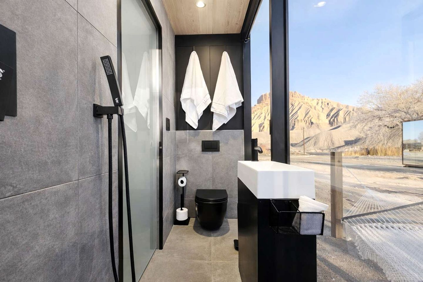 A modern bathroom with a glass shower enclosure, a black toilet, a white sink, and towels hanging on a rack.