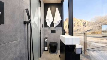 A modern bathroom with a glass shower enclosure, a black toilet, a white sink, and towels hanging on a rack.