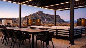 Um pátio externo com mesa e cadeiras de madeira, um sofá e uma pequena estrutura de madeira com luzes.