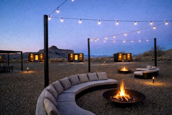 A semi-circular outdoor seating area with a fire pit, string lights, and a view of the desert landscape.