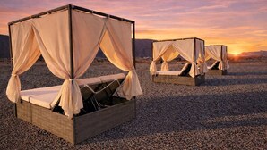 Zwei schlaffreundliche Betten mit Baldachin, aufgeständert auf Kies, mit Sonnenuntergang im Hintergrund.