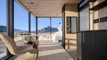 Un intérieur moderne avec de grandes fenêtres, un lit, des fauteuils en osier et une vue sur une montagne.