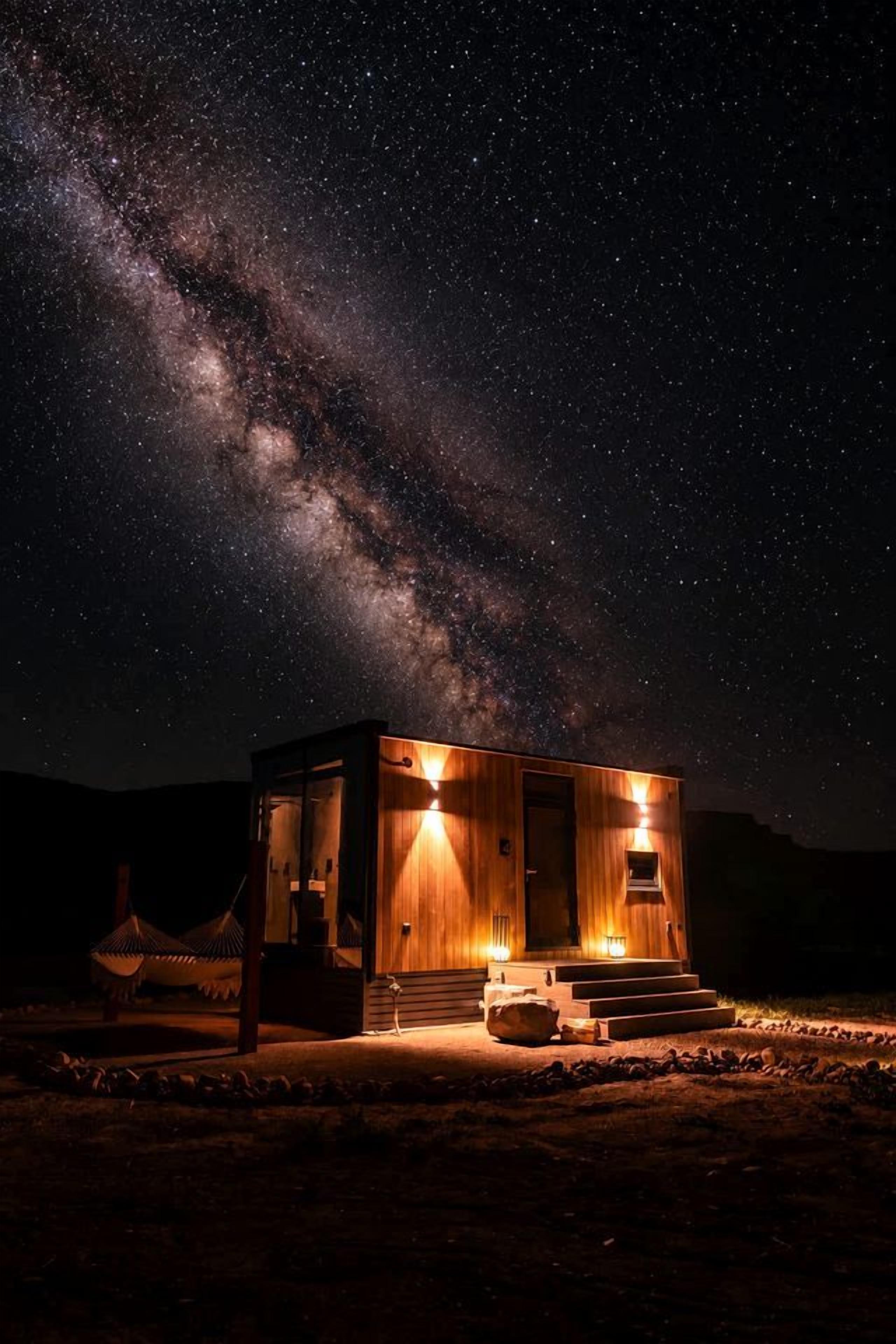 Una cabaña pequeña e iluminada con fachada de madera, ubicada en un entorno natural bajo un cielo estrellado.