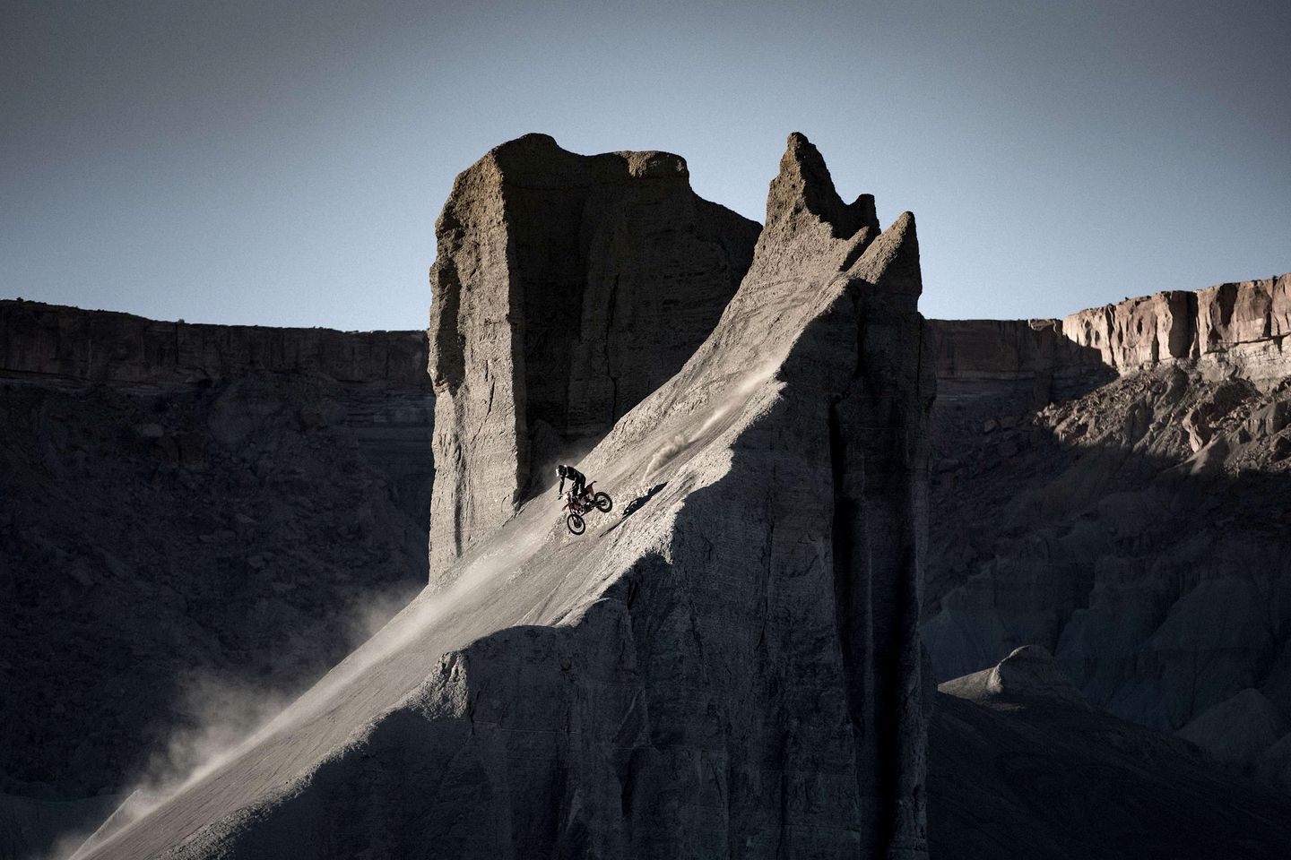 A mountain biker on a steep, rocky slope with a clear sky.