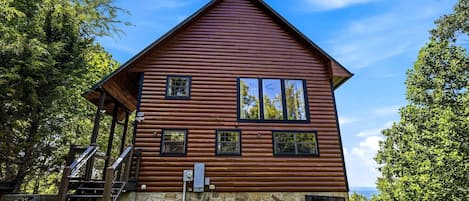 A wooden cabin with a stone foundation, a porch, and a staircase leading to the entrance.