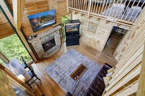 Interior de una cabaña con chimenea de piedra, un televisor montado en la pared y una consola de videojuegos.
