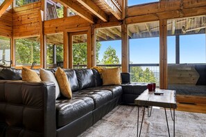 A spacious room with a large leather sofa, a wooden coffee table, and large windows offering a view of the outdoors. - Stunning Mountain View Cabin with Hot Tub & Game Room near Pigeon Forge, Sevierville TN (Sevierville)