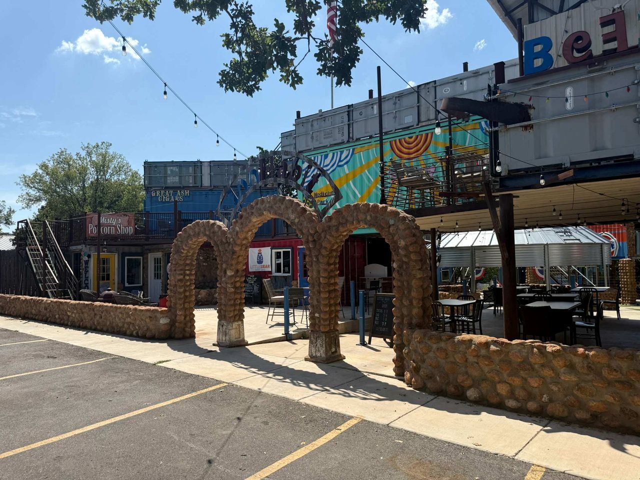Un estacionamiento con un edificio que presenta un mural, una tienda de palomitas de maíz y mesas al aire libre.
