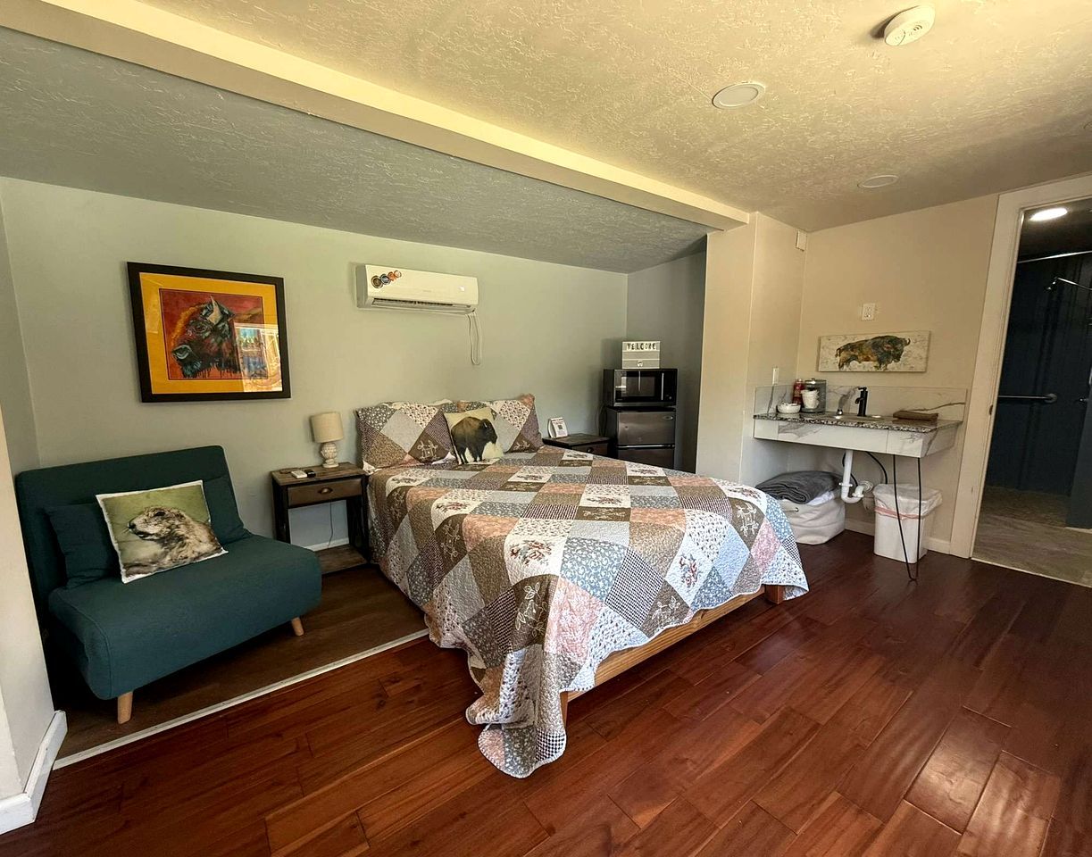 A bedroom with a bed, a desk, a chair, and a painting on the wall.