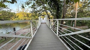 Un puente peatonal de madera con barandillas blancas que cruza un cuerpo de agua, rodeado de árboles.