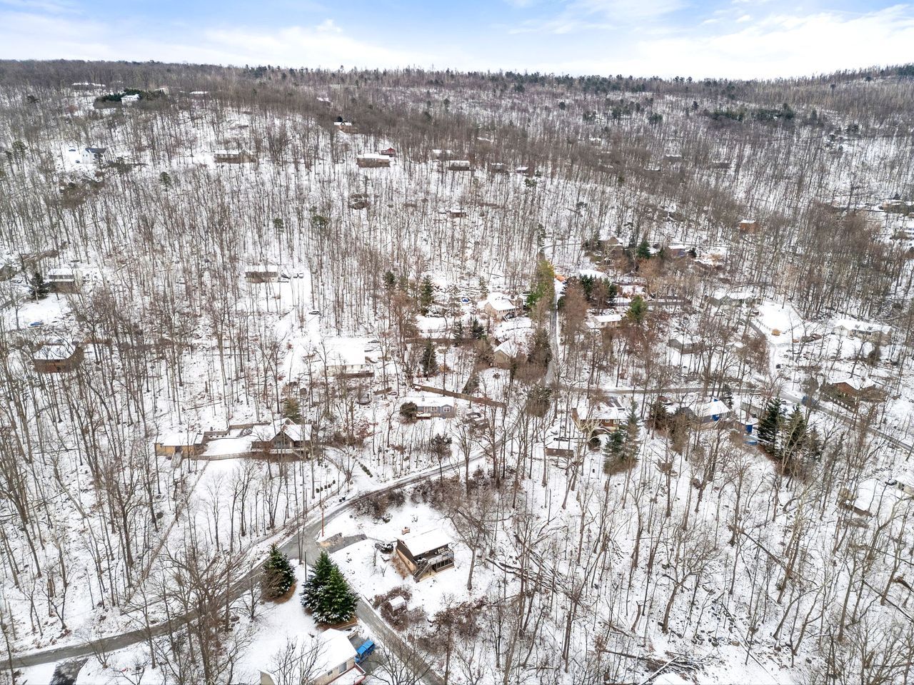 An aerial view of a snow-covered residential area with houses, roads, and a few trees.