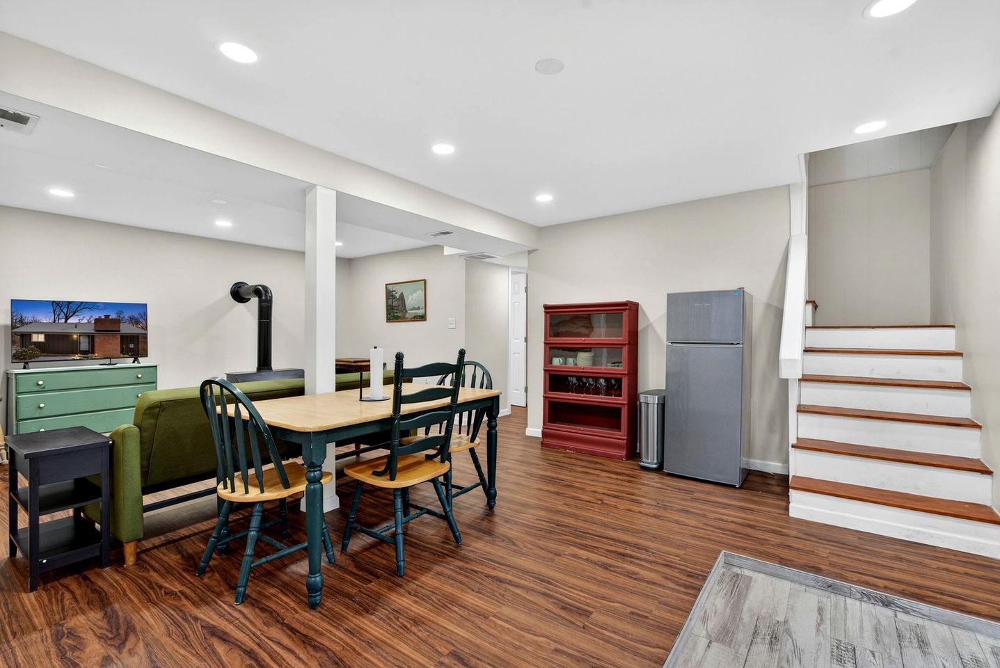 A modern kitchen with a dining area, wooden flooring, and a staircase.