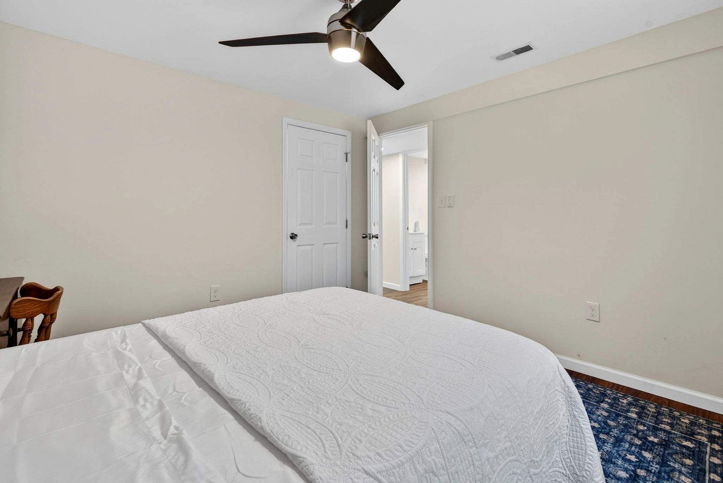 Un dormitorio con cama, ventilador de techo, una puerta y vista a otra habitación.