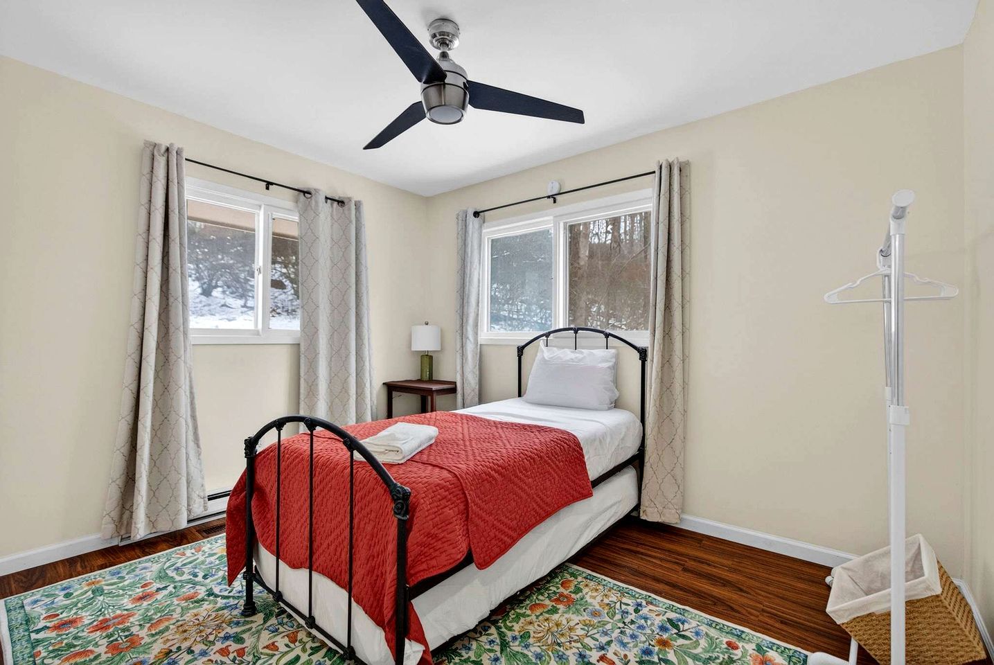 Ein Schlafzimmer mit einem Bett, Deckenventilator, Fenster, Nachttisch und Stehlampe.
