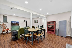 A dining area with a wooden table and chairs, a green sofa, a red bookshelf, and a grey refrigerator. - Spacious Mountain Retreat with Hot Tub & Screened Porch Near Wineries and Appalachian Trail | Harpers Ferry, WV (Harpers Ferry)