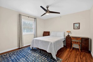 Un dormitorio con cama, escritorio, silla, ventilador de techo y ventana.