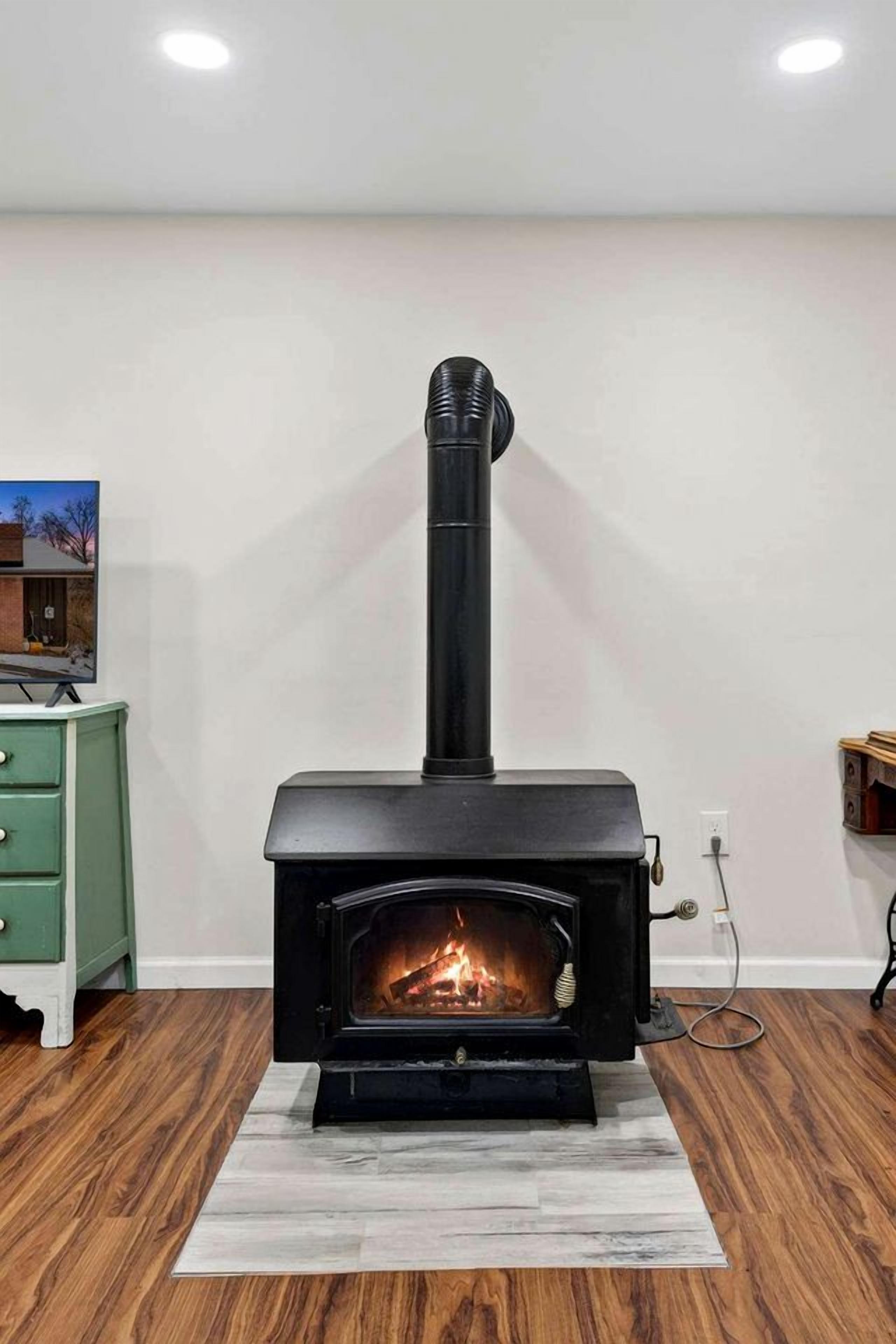 A wood-burning stove in a room with a green dresser, a white wall, and wooden flooring.