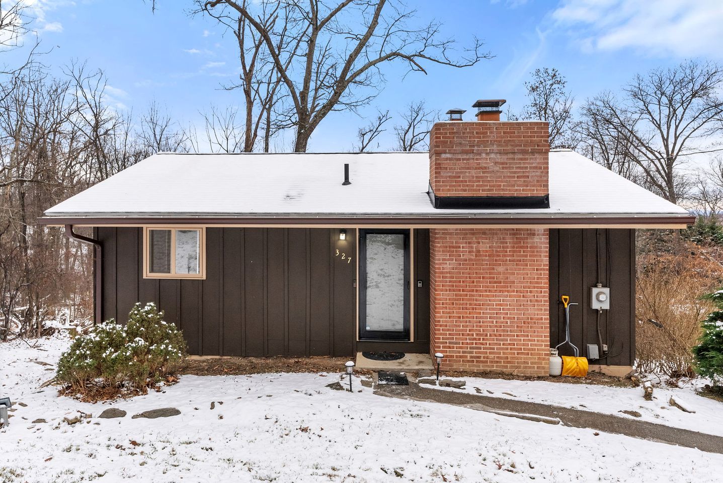 A single-story house with a dark brown exterior, a brick chimney, and a small window.