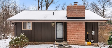 A single-story house with a dark brown exterior, a brick chimney, and a small window.
