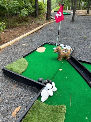 A miniature golf course with a green artificial turf, a red flag, and a small dog statue. - Electrifying Family Cabin with Mini Golf, Arcades & EV Charger Near Beavers Bend State Park | Broken Bow, Oklahoma (Broken Bow)
