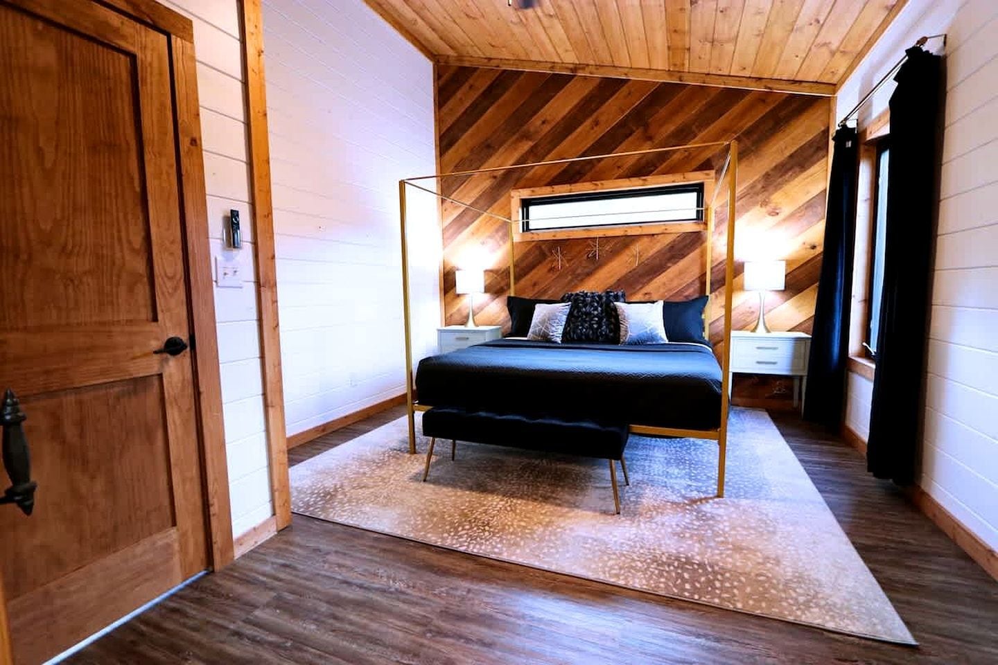 Un dormitorio con techo inclinado, una cama con dosel, mesitas de noche y un ventanal grande.