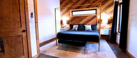 Un dormitorio con techo inclinado, una cama con dosel, mesitas de noche y un ventanal grande.