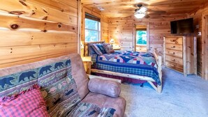L’intérieur d’un chalet en bois, avec un lit, un canapé, une commode et un téléviseur.