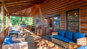 A log cabin with a covered porch, a grill, a sofa, and a dining area.