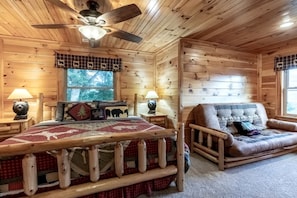 Quarto de cabana de tronco com uma cama, uma cadeira, uma janela e um ventilador de teto.