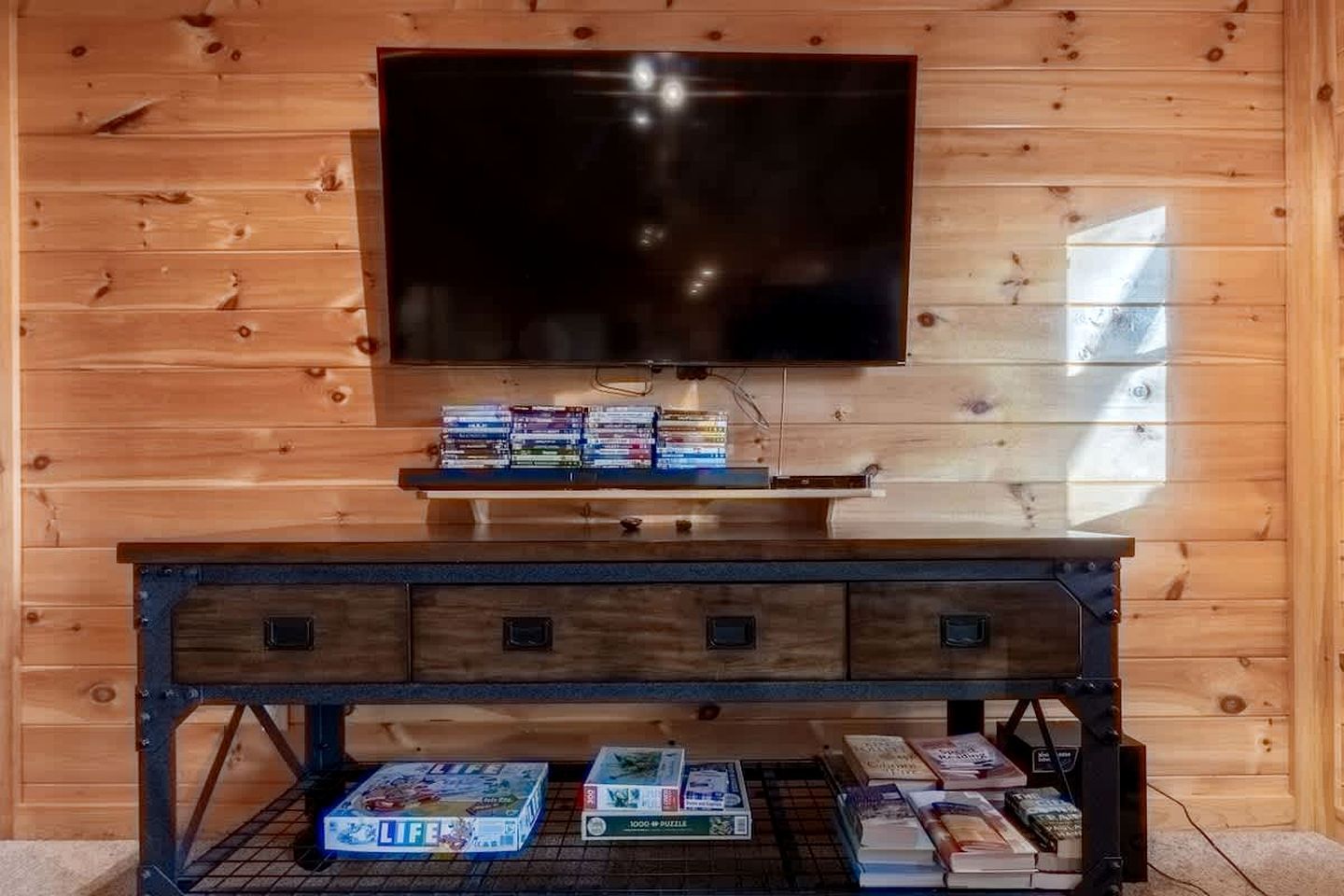Ein Holzinterieur mit einem Fernseher, der über einer dunklen Holzunterhaltungsecke angebracht ist, in der sich Videospiele und Bücher befinden.