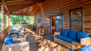 Une cabane en rondins dotée d’un porche couvert, d’un barbecue, d’un canapé et d’un coin repas.