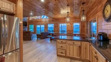 A wooden cabin interior with a kitchen, dining area, and a view of the outdoors.