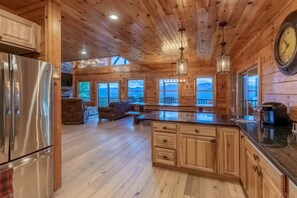 Interior de uma cabana de madeira com cozinha, sala de jantar e vista para o exterior.