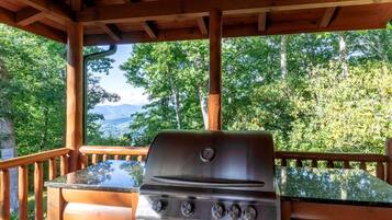 Een barbecue op een terras met uitzicht op een bos en bergen.