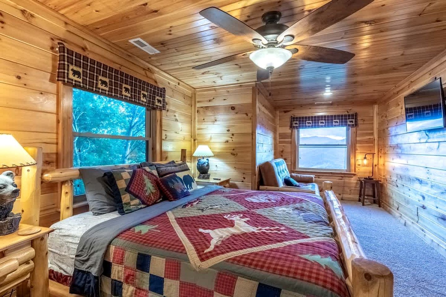 A wooden cabin bedroom with a bed, a chair, a desk, and a window with a view.