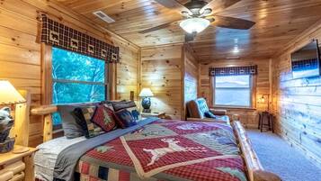 A wooden cabin bedroom with a bed, a chair, a desk, and a window with a view.